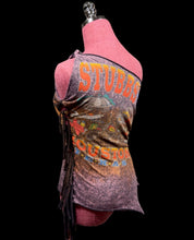 Load image into Gallery viewer, A sleeveless wrap-style top displayed on a pink dress form against a black background. The garment features a distressed purple and brown base with orange 'STUBBS' lettering and a central graphic print.
